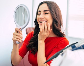 Woman in red shirt smiling at reflection in handheld mirror
