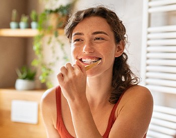 Woman smiling while brushing her teeth in bathroom