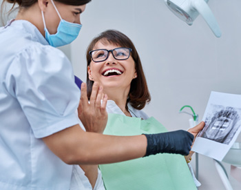 Woman smiling with dentist while reviewing X-ray