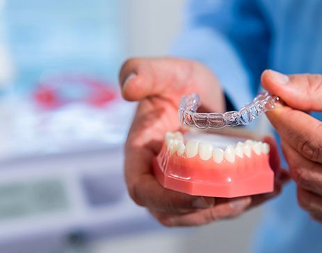Dentist placing clear aligner on model of teeth