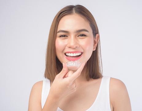 Woman smiling while holding clear aligner