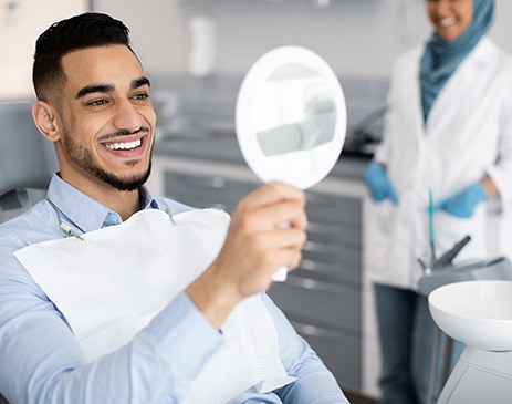 Man smiling at reflection in handheld mirror