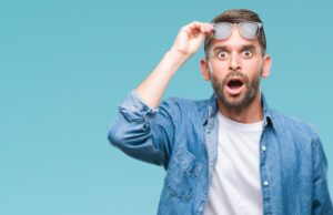 Man with surprised expression on his face raising his sunglasses.