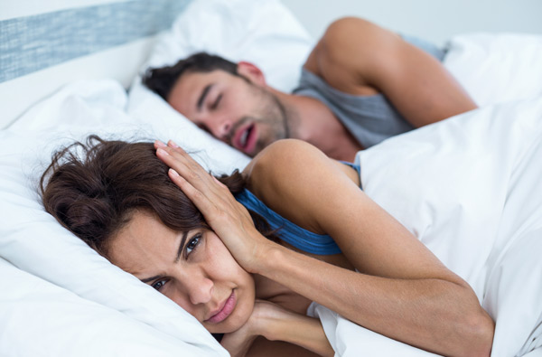 Woman covering ears while husband snores.